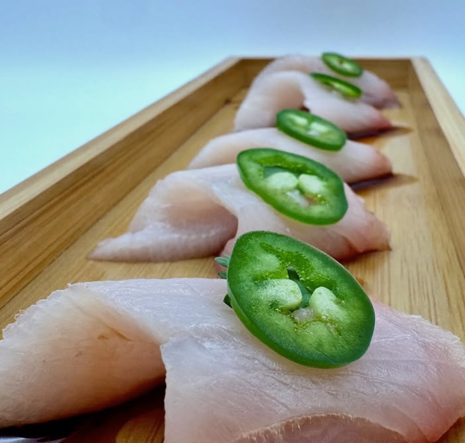 Hamachi sashimi with jalapeño, sliced and plated on a wooden board